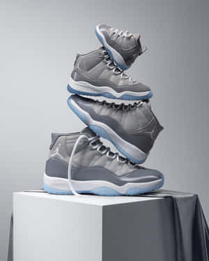 在工作室環境中，灰色和藍色 Jordan 11 波鞋堆疊在白色底座上。