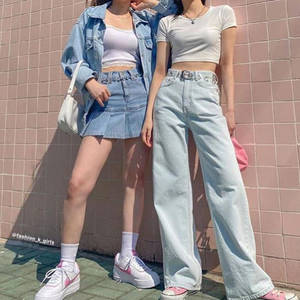 兩位穿著牛仔服飾和粉紅色運動鞋的年輕女性站在粉紅色瓷磚牆前。