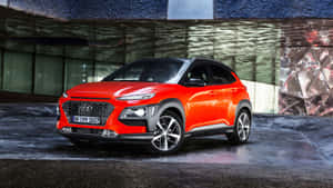 一輛明亮的橙色Hyundai Kona SUV停在一棟現代建築前。 — 現代汽車 壁紙
