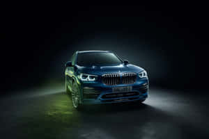 藍色BMW X5 Alpina SUV在黑暗攝影棚中被聚光燈照亮，帶有綠色地板光芒。 — MacBook Pro M2 壁紙
