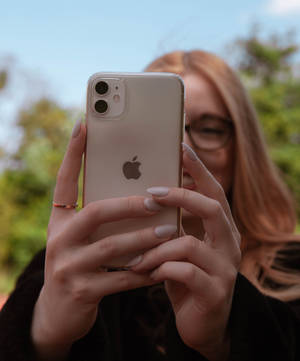 戴眼鏡和淺棕色頭髮的人拿著金色iPhone 11在戶外自拍。