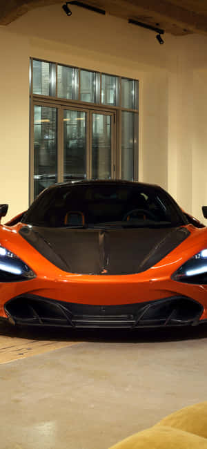 橙色McLaren跑車在帶有大窗戶的現代室內車庫中展示。 — iPhone 17 Pro 壁紙