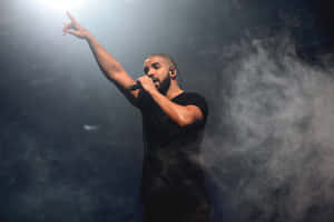 Drake 在聚光燈下煙霧彌漫的舞台上對著麥克風唱歌。