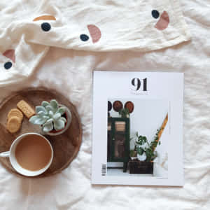 舒適的床上場景，有茶餅、多肉植物和雜誌，放在圖案床單上。 — iPad (A16) 壁紙
