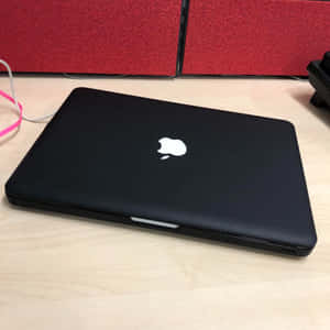 關閉的黑色MacBook在木桌上，後面有紅色圖案牆板。