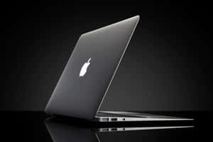 在暗色工作室燈光下，反射黑色表面上的時尚銀色 MacBook 筆記型電腦。