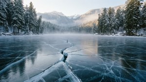 結冰的湖面佈滿裂紋，周圍是雪覆蓋的松樹和山巒。
