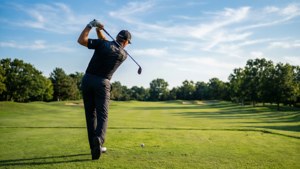 高爾夫球手在陽光明媚的高爾夫球場上揮桿，綠草如茵，樹木環繞