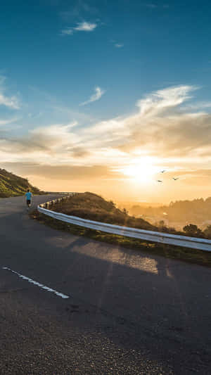 一個人在金色夕陽下沿著彎曲的山路奔跑。 — 日落大道 壁紙