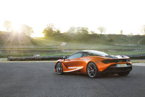 日落時分賽道上的橙色McLaren跑車，背景是綠色山丘。 — 4K 法拉利 壁紙