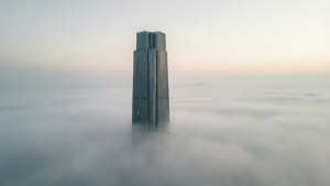 黎明時分，一座高聳的玻璃摩天大樓聳立於雲海之上
