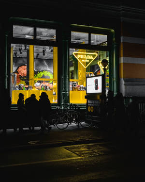 夜晚在燈光明亮的 Prada 商店外的人和自行車剪影。
