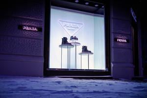 Prada 商店櫥窗在雪夜城市中展示鞋子。