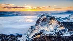 黑色沙灘上夕陽下發光的冰塊與海浪