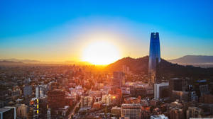 夕陽下密集的城市，有一座高玻璃塔和遠山。 — 建築 壁紙