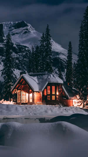 舒適的小屋在雪夜中發光，周圍環繞著山脈和樹木 — 冬天 壁紙