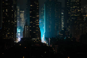 夜晚的城市景觀，有燈火通明的摩天大樓和一道藍色光束。 — 夜景城市 壁紙
