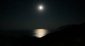 月光在夜間反射在海面上，星空和黑暗的山丘。