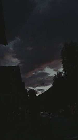 黃昏時分的黑暗城市天際線，上方有戲劇性的雲層 — 深色iPhone壁紙