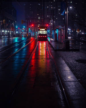一輛電車在濕漉漉的夜晚城市街道上行駛，反射著紅色和藍色的霓虹燈光。 — 暗夜城市 壁紙