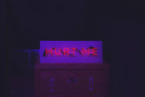 黑暗中的木箱上寫著 hurt me 的紅色霓虹燈牌 — 深色iPhone壁紙