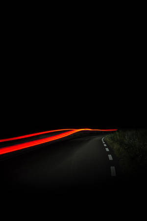 來自汽車的紅色光軌沿著夜晚黑暗蜿蜒的道路彎曲。