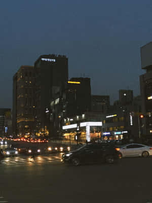 黃昏時分的城市街道，有汽車和發光的建築物。 — 夜晚 GIF 壁紙