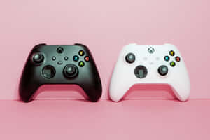 粉紅色表面上兩個黑色和白色的Xbox遊戲控制器。