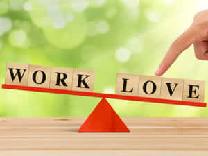手傾斜紅色天秤，在木質表面上平衡「work」和「love」積木。