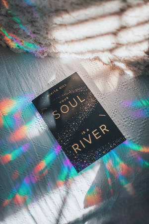 一本名為《Your Soul Is a River》的書放在一個有紋理的表面上，帶有彩色光圖案。