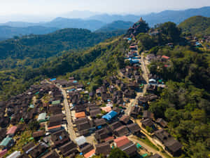 山村，房屋沿著林木茂密的山坡向上攀爬，通往山頂的一座寺廟。