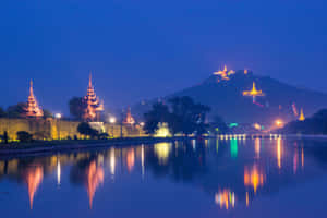 夜晚景色，發光的寶塔倒映在水中，背景是山脈。