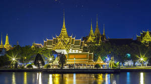 夜晚燈光下的金色寺廟建築群，星空與水面倒影。