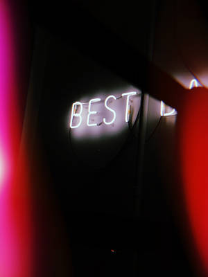 一個發光的白色霓虹燈牌，在黑暗的房間中顯示「BEST」，伴有紅色光暈。