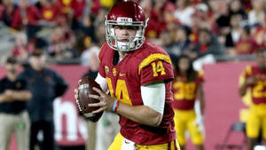 身穿紅金配色制服的USC美式足球四分衛在夜間比賽中持球。 — NFL 美式足球 GIF 壁紙