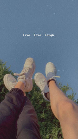 兩個人的腳穿著白色運動鞋指向藍天，有綠樹和文字 live love laugh。