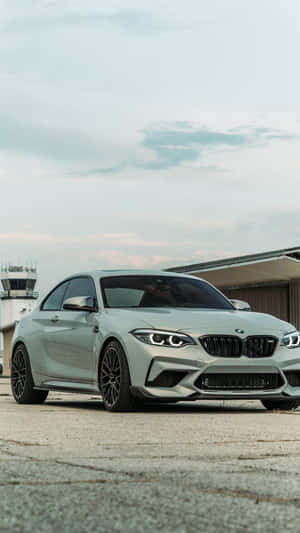銀色BMW M2跑車在多雲的日子停泊在機場控制塔附近。 — iPhone 8 壁紙