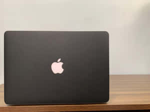 黑色MacBook手提電腦放在木桌上，白色牆壁背景