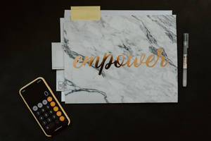 雲石文件夾帶金色箔片 'empower' 文字，旁邊有計算機和筆在黑色桌上。