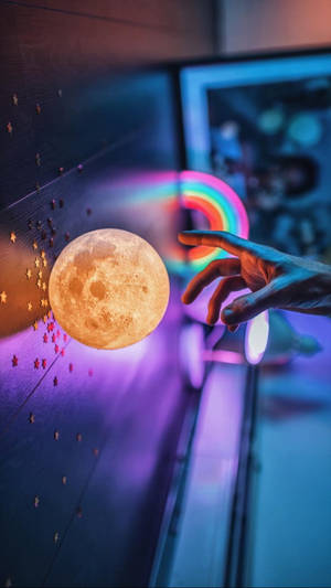 手伸向帶有彩虹光環和星星的發光月亮燈。 — 霓虹 iPhone 壁紙