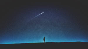 一個人在夜晚站在山丘上，伸手去抓星空中的流星。 — 月光 壁紙