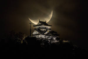 一座傳統的日本城堡在夜晚被照亮，背後有一彎新月。