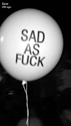 一個白色氣球，上面以粗體黑色字寫著 sad as fuck，背景昏暗。