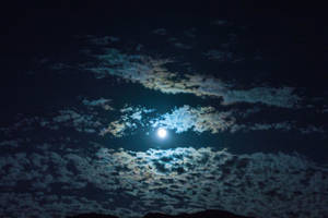 滿月在黑暗夜空中有紋理的雲層後發光。