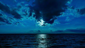 月光穿過雲層，照耀在平靜的海洋上。 — 月光 壁紙