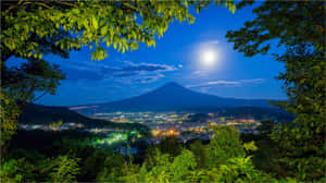 富士山上空的滿月，夜間被綠樹環繞的發光城市燈光 — 日本 壁紙