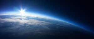 從太空看到地球上的日出，顯示藍色大氣層、白雲和下方的黑暗海洋