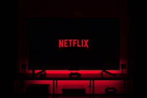 電視屏幕顯示Netflix標誌，帶有紅色背光，黑暗房間的支架上有遊戲控制器。 — Netflix GIF 壁紙
