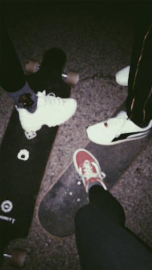 夜晚，三個人穿著運動鞋站在滑板上的人行道上。 — 滑板少年美學 壁紙