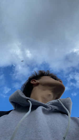 穿著灰色連帽衫的年輕男子抬頭看著有雲和飛鳥的藍天。